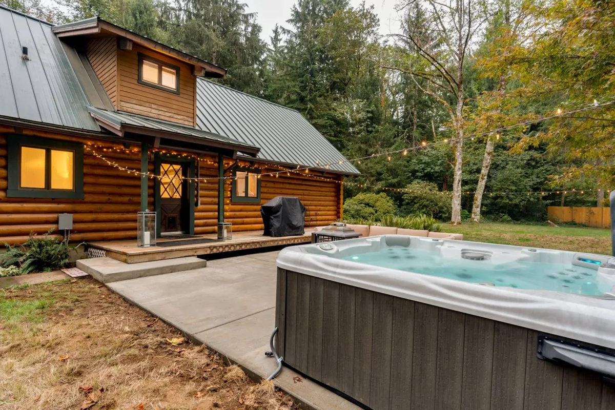 This scene spotlights a cozy hot tub set beside a wooden exterior, artfully lit with string lights. The landscaped garden and open sky enhance the sense of privacy and an invitation to unwind under the stars.