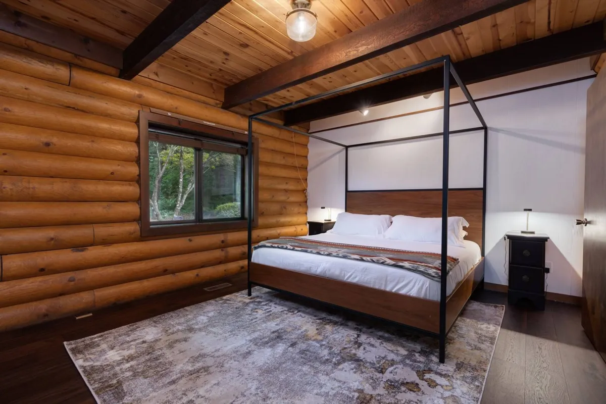 A tranquil bedroom featuring a four-poster bed against wooden log walls, with a window offering a view of the outdoors. The room exudes warmth, relaxation, and privacy, perfect for unwinding after a long day.