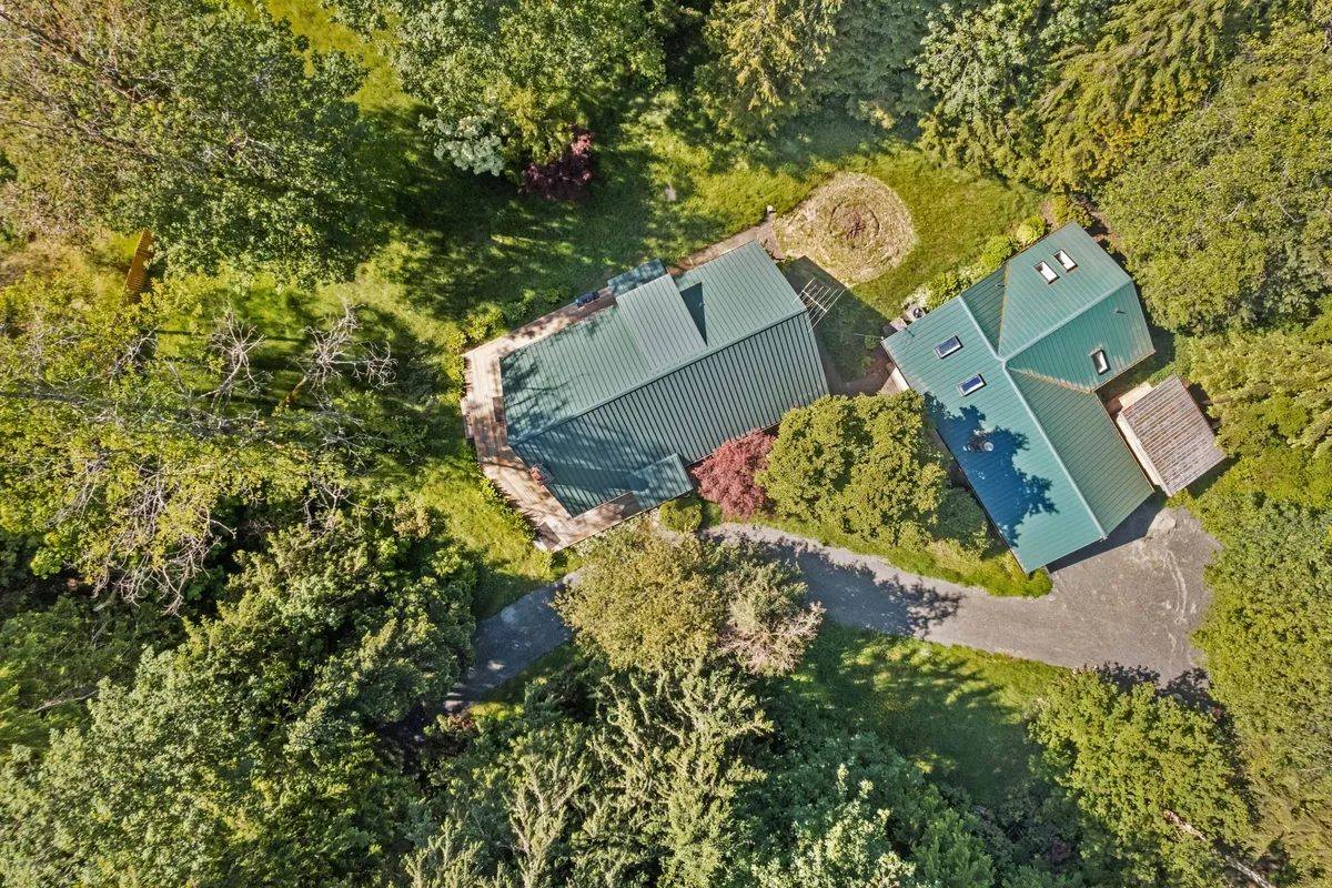 A circular patio area is tucked among mature trees, with green-roofed houses as a backdrop. The patio is designed for gatherings, outdoor dining, and leisure, all framed by abundant natural scenery.