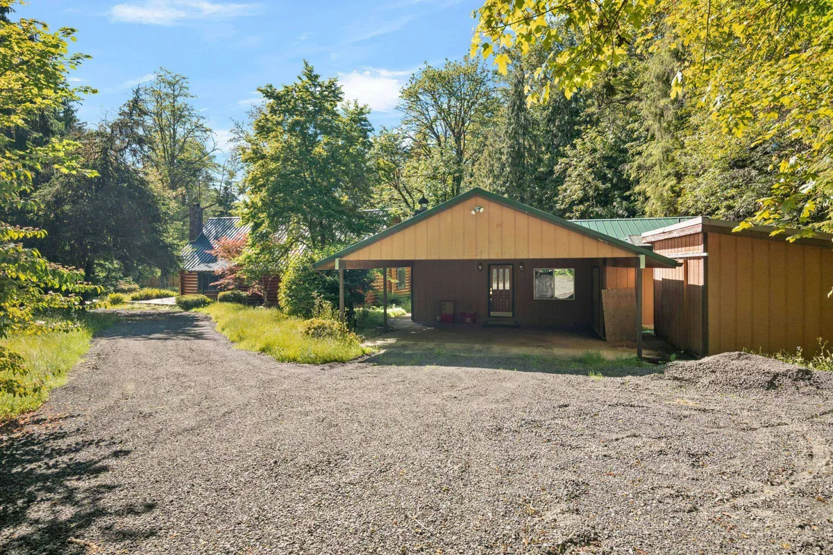 This peaceful exterior image captures the main house nestled amongst tall trees, with a gravel path leading up to it. The inviting porch hints at mornings spent with coffee or evenings watching the sun rise or set, all while embraced by nature.