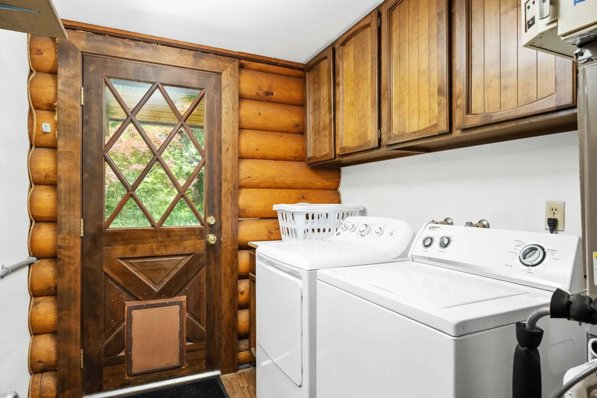 A practical laundry space with a washing machine, wooden door, storage cabinets, and views of the surrounding garden. The area feels cozy and functional, making chores more convenient for guests seeking longer stays or extra independence.