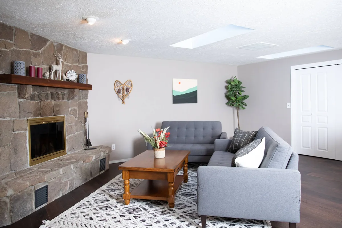 Inside, a warm, cozy living room is centered around a stone fireplace, with comfortable sofas and tasteful artwork. The inviting seating offers the perfect space to gather for laughter, stories, or a quiet evening after a day outdoors.