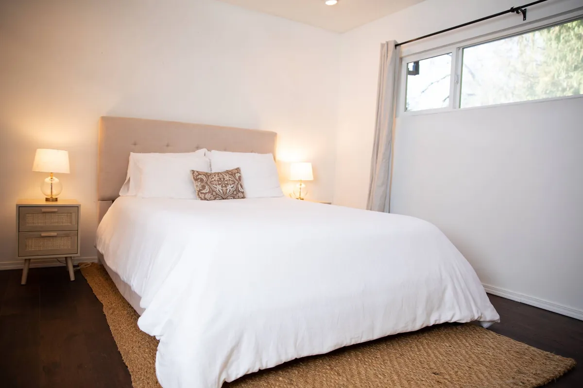 A serene and spacious bedroom with a plush queen bed, flanked by nightstands and lamps. Soft natural light filters in, creating a tranquil atmosphere ideal for restful nights, quiet reading, or simply unwinding in privacy.