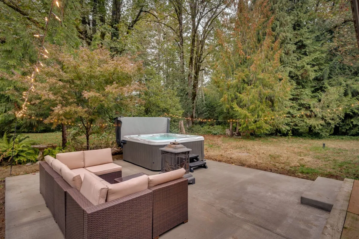 A bubbling hot tub set within a landscaped outdoor seating area, surrounded by greenery. The space is designed for relaxation, with comfortable seating inviting guests to unwind after a day of activities. The natural environment and clear sightlines to the sky evoke outdoor living.